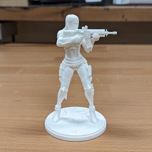 May include: A white 3D-printed figurine of a female character holding a rifle. The figure is standing on a circular base. The character is wearing a form-fitting outfit with armor details.