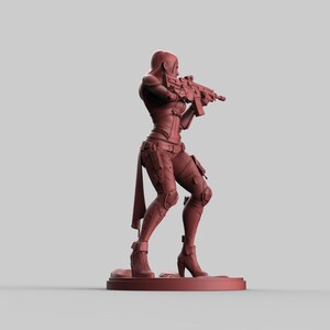 May include: A reddish-brown figurine of a female character in a combat pose, holding a rifle. The figure is wearing a form-fitting outfit with knee pads and boots. The figurine is standing on a small, circular base.
