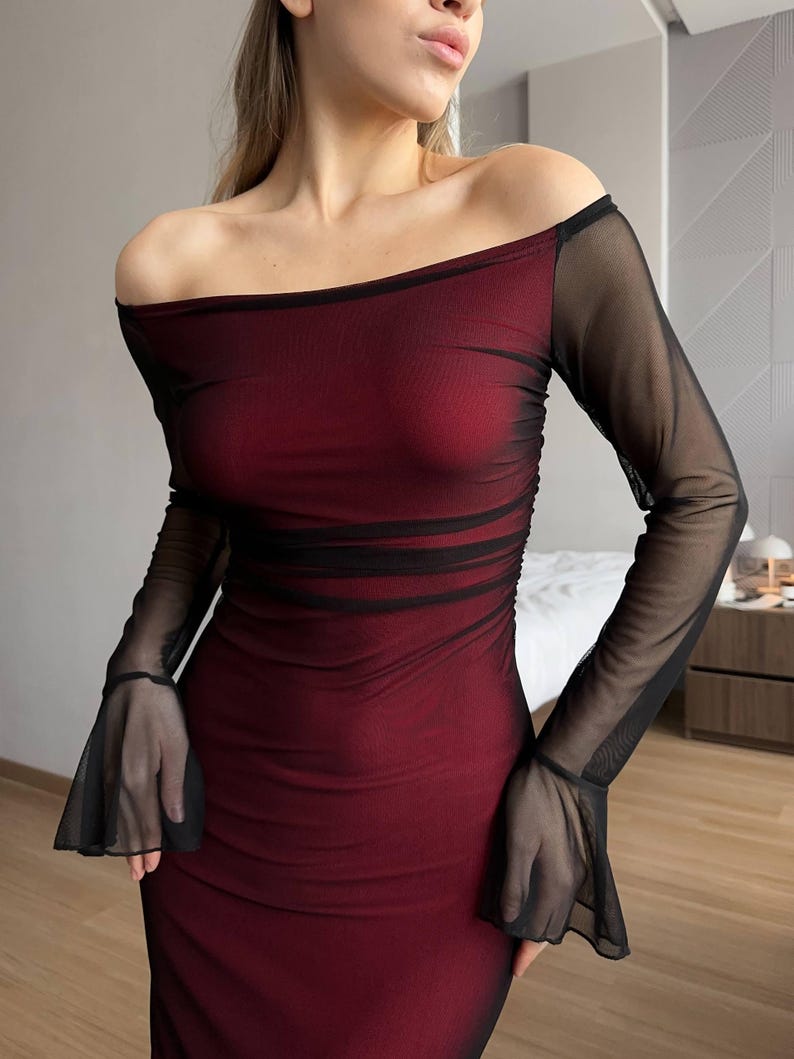 May include: A long-sleeved off-the-shoulder dress featuring a deep red base layer with a sheer black mesh overlay. The garment includes ruched detailing across the torso and flared bell sleeves at the wrists, creating a layered appearance.