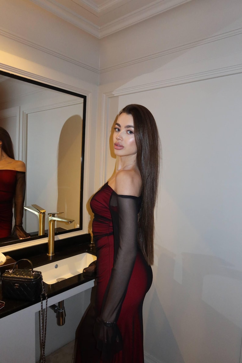 May include: A form-fitting, off-the-shoulder dress featuring a deep red base layer with a sheer black mesh overlay. The garment includes long, sheer black mesh sleeves and a straight neckline that exposes the shoulders and upper chest area.