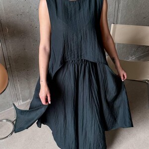 May include: A dark charcoal sleeveless top and matching skirt set featuring a crinkled, textured fabric. The top has a round neckline and a high-low hemline, while the skirt has an elasticized waistband and a loose, flowing silhouette.