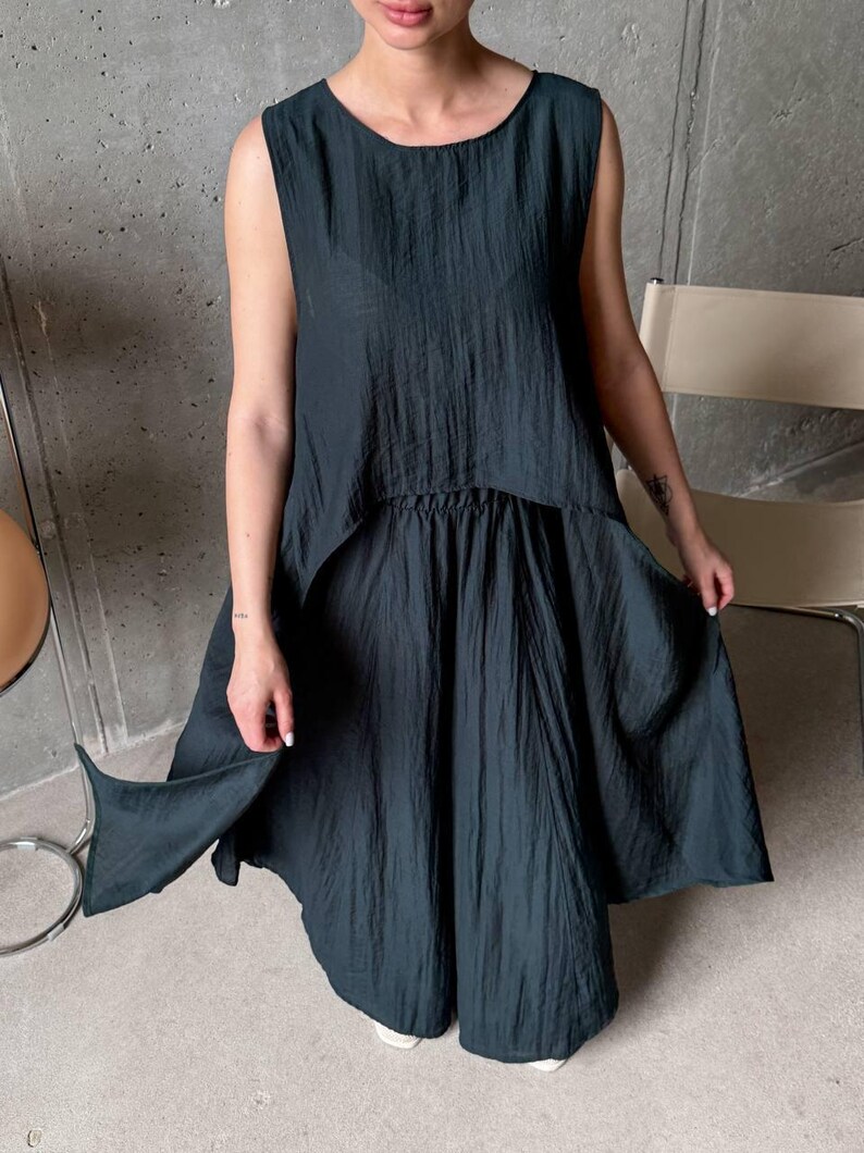 May include: A dark charcoal sleeveless top and matching skirt set featuring a crinkled, textured fabric. The top has a round neckline and a high-low hemline, while the skirt has an elasticized waistband and a loose, flowing silhouette.