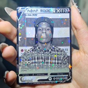 Puede incluir: Una tarjeta coleccionable con una imagen en blanco y negro de A$AP Rocky. La tarjeta tiene un diseño holográfico con texto que incluye "Live. Love. ASAP" y "2011". La tarjeta también tiene una sección "Bass" y "Peso".