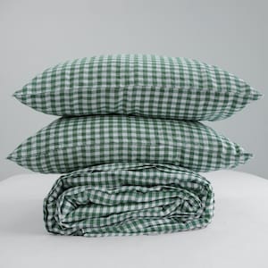 May include: Three pieces of bedding: two pillows and a folded blanket. The pillows and blanket feature a green and white gingham pattern. The items are stacked on top of each other, with the blanket at the bottom.