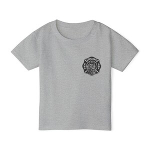 May include: A heather grey short-sleeve t-shirt featuring a black and white circular graphic on the left chest. The graphic depicts a firefighter emblem with the text LIVE OAK ENG ONE and a central illustration of a firefighter in gear.