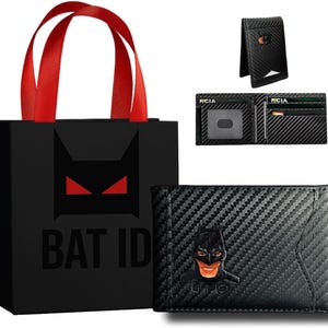 Może przedstawiać: Czarny portfel z wzorem z wł&oacute;kna węglowego, z emblematem Batmana. Portfel jest prezentowany z pasującą torbą na prezent z logo Batmana i napisem "BAT ID". Dodatkowe widoki pokazują klips na pieniądze i wnętrze portfela.