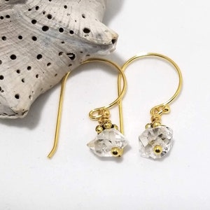 Puede incluir: Un par de pendientes de oro con cristales de cuarzo transparentes y cuentas doradas. Los pendientes son de estilo colgante con un aro de oro simple.