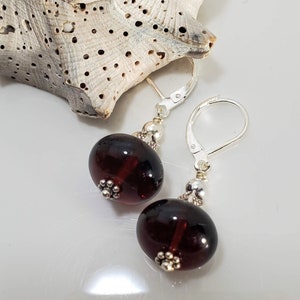 May include: A pair of dangle earrings with dark red glass beads and silver accents. The earrings have lever back closures.