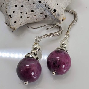 May include: A pair of dangle earrings with silver hooks and purple gemstone beads.