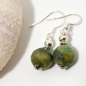 Peut inclure: Une paire de boucles d'oreilles en argent avec des perles de pierres précieuses vertes et roses. Les perles sont rondes et ont une surface texturée.