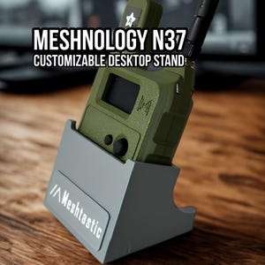 May include: A grey desktop stand with the text Meshtastic printed on the front, holding an olive green electronic device with an antenna. The text Meshnology N37 Customizable Desktop Stand is visible at the top of the image.