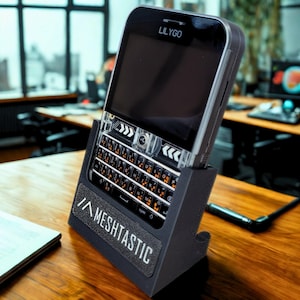 May include: A LILYGO T-Deck device with a black screen and a QWERTY keyboard, resting in a dark grey 3D-printed stand. The stand features the white text MESHTASTIC printed on the front. The device has a clear plastic casing around the keyboard area.