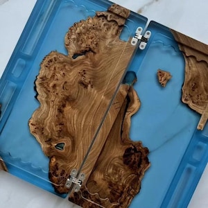 May include: A handcrafted, two-part tray with a vibrant blue resin base and intricate wood grain details. The wooden sections are connected by metal hinges, creating a unique and functional design. The wood has a natural, warm brown color.