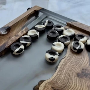 May include: A backgammon set with a wooden frame and a gray playing surface. The game pieces are black and white, arranged on the board. The wooden frame has a natural wood grain.