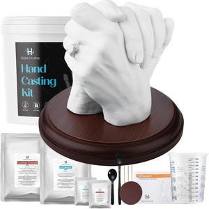 May include: A white hand casting kit with a finished hand sculpture on a wooden base. The kit includes casting powder, alginate, mixing tools, and a measuring cup. The text on the kit reads "Hand Casting Kit" and "Hula Home".