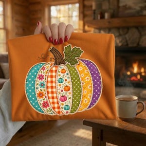 Puede incluir: Un artículo de tela color naranja quemado con una gran aplicación central de calabaza. La calabaza está compuesta por segmentos verticales con diversos patrones, incluyendo estampados florales, cuadros vichy naranjas, lunares y motivos.