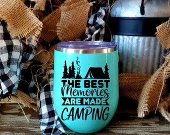Op de afbeelding: Een turquoise roestvrijstalen tumbler met een zwart ontwerp met de tekst "The Best Memories Are Made Camping". De tumbler heeft een paarse deksel en staat op een houten oppervlak.