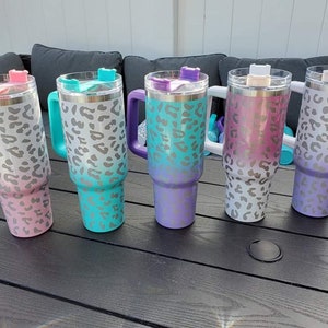 May include: Five stainless steel travel mugs with a leopard print design. The mugs are in different colors: pink, teal, purple, white, and lavender. Each mug has a lid with a handle.