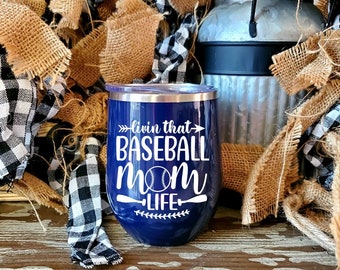 Op de afbeelding: Een blauwe roestvrijstalen tumbler met een wit ontwerp met de tekst "Livin' that Baseball Mom Life" met een honkbal en twee honkbalknuppels.