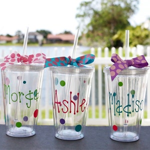 Op de afbeelding: Drie doorzichtige plastic bekers met rietjes en gepersonaliseerde namen, "Morgan", "Ashle" en "Madison", versierd met kleurrijke stippen en strikken.