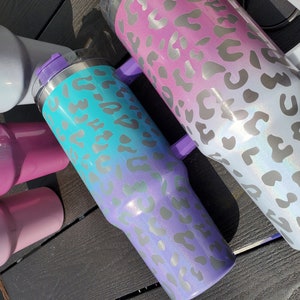 May include: Three stainless steel tumblers with a leopard print design. The tumblers are ombre, with a light blue, pink, and white color gradient.