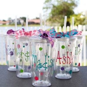 Op de afbeelding: Zes doorzichtige plastic bekers met rietjes en kleurrijke stippenboogjes. Op elke beker staat een naam: "Brian", "Lori", "Madison", "Ashlie", "Bailie" en "Olivia".