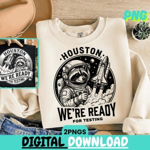 Könnte beinhalten: Cremefarbenes Sweatshirt mit einem schwarz-weißen Aufdruck eines Waschbären im Raumanzug, einer Rakete und dem Text "Houston, We're Ready for Testing." Ein kleineres Bild des Designs befindet sich auf einem schwarzen T-Shirt. Die Worte "Digital Download" stehen unten.