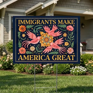 May include: A rectangular yard sign with the text "IMMIGRANTS MAKE AMERICA GREAT" in gold lettering. The sign features a floral and bird design in shades of pink, orange, and green against a dark blue background. The sign is held up by a metal stake.