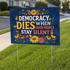 May include: A navy blue yard sign with the text "DEMOCRACY DIES WHEN GOOD PEOPLE STAY SILENT" in white and yellow. The sign is decorated with colorful flowers, butterflies, and a bee. The sign is held up by two metal stakes and is placed in a grassy yard.