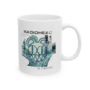 May include: White ceramic mug featuring the band name "RADIOHEAD" and the album title "OK COMPUTER". The mug has a blue and white graphic design of a bear-like face with a cityscape background.