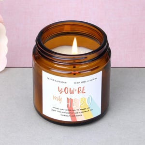 Può includere: Una candela accesa alla lavanda in un barattolo di vetro marrone. L'etichetta recita "You're my Hero" con un messaggio personalizzato. La candela ha un tempo di combustione di 16 ore.