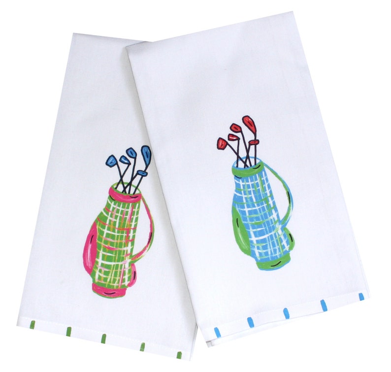 May include: Two white kitchen towels with a green, pink, and blue plaid golf bag design. Each towel has a different color golf club design.