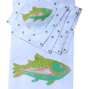 May include: Set of four white linen napkins with green polka dots and a green and pink fish design. The napkins are folded and stacked on top of a larger white linen napkin with a larger green and pink fish design.