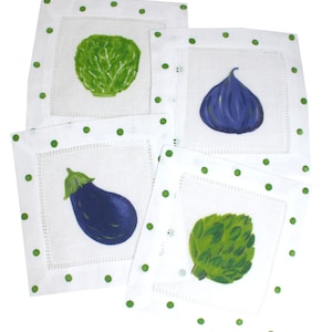 May include: Set of four white linen napkins with green polka dots and a different painted vegetable on each napkin: a green artichoke, a green cabbage, a purple eggplant, and a purple fig.