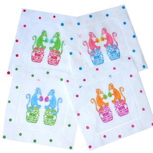 May include: Set of four white linen napkins with a colorful monkey design. Each napkin features two monkeys sitting on a jar, drinking from a cup. The napkins have a polka dot border in various colors.