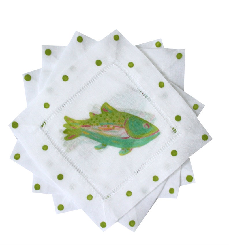 May include: Set of four white linen napkins with green polka dots and a green and blue fish illustration in the center.