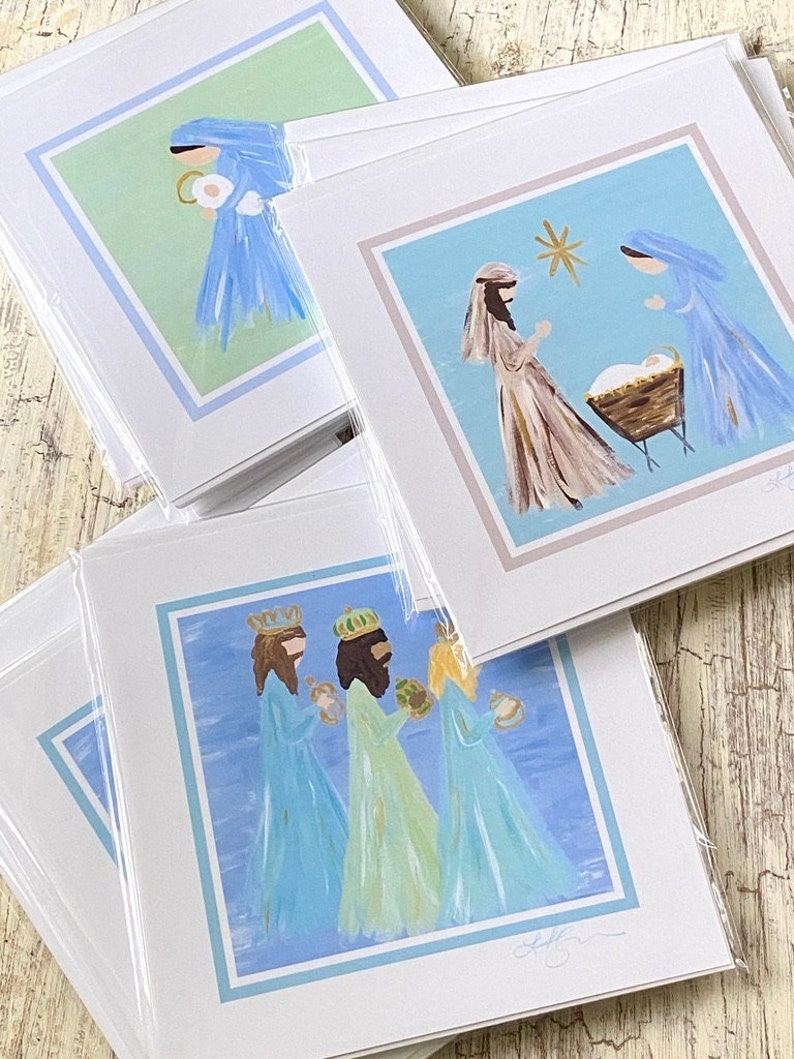 May include: Set of three Christmas cards featuring hand-painted illustrations of the Nativity, the Three Wise Men, and the Angel Gabriel. The cards are printed on white cardstock with a blue border.