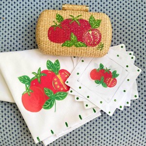 Puede incluir: Un bolso de mano tejido, servilletas y posavasos blancos con un dise&ntilde;o de tomate y albahaca. El bolso de mano tiene forma rectangular con textura tejida y cierre dorado. Las servilletas y posavasos tienen un borde punteado verde.
