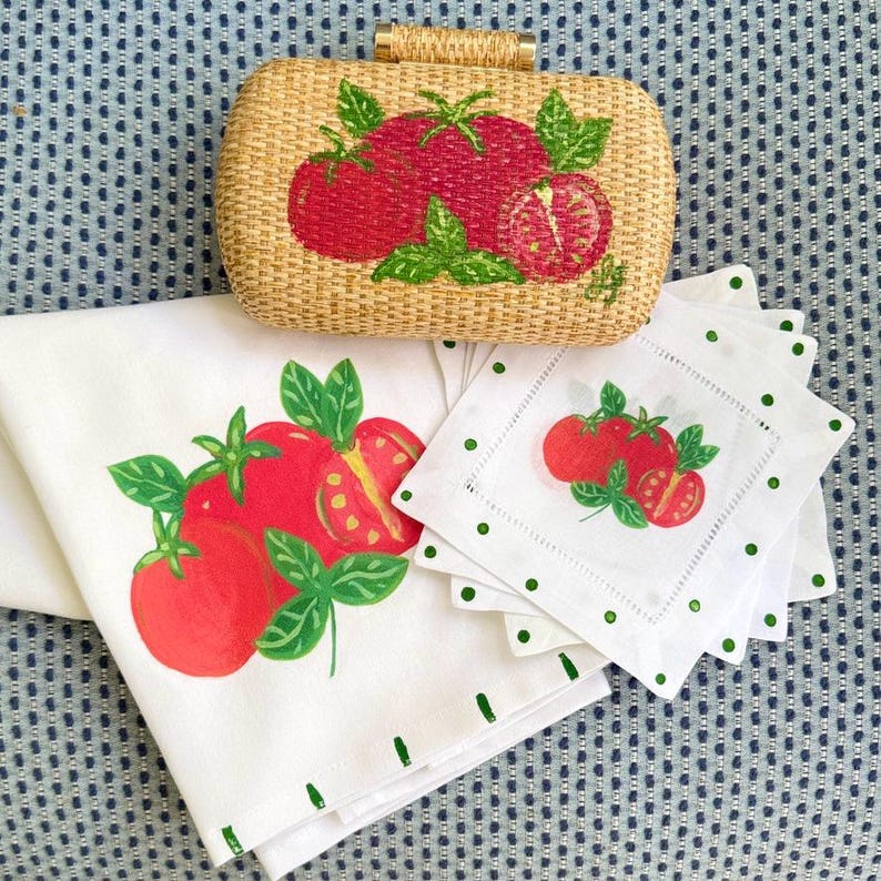 Puede incluir: Un bolso de mano tejido, servilletas y posavasos blancos con un dise&ntilde;o de tomate y albahaca. El bolso de mano tiene forma rectangular con textura tejida y cierre dorado. Las servilletas y posavasos tienen un borde punteado verde.