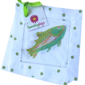 May include: Set of four white linen napkins with green polka dots and a green and blue fish design. The napkins are trimmed with white stitching. A green ribbon with a white polka dot pattern is tied around the napkins with a tag that reads "lemondaisydesign".