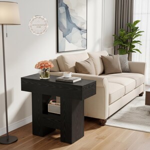 May include: A black wood grain side table with a rectangular top and a central open storage shelf. The table features a thick, sturdy base design and a smooth finish, providing a functional surface for small items in a living space.