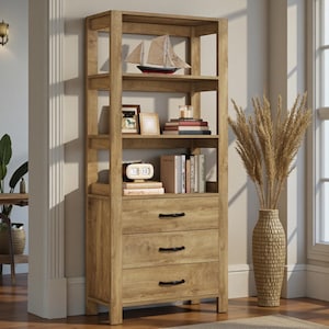 May include: A wooden bookshelf with three drawers and open shelves. The shelves display books, framed pictures, a decorative sailboat, and a small clock. The bookshelf is made of light brown wood and has black drawer pulls.