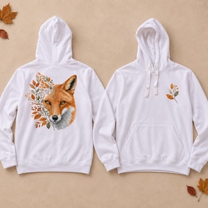Könnte beinhalten: Ein weißer Kapuzenpullover mit einer großen Grafik eines Fuchskopfes, der mit Herbstblättern auf der Rückseite integriert ist, sowie einem kleineren passenden Blattzweig-Motiv auf der linken Brust. Der Hoodie hat eine Kängurutasche und Kordelzüge.