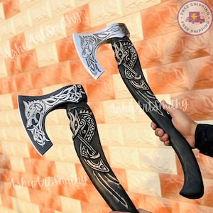 May include: Two Viking-style axes with intricate carvings. The axe heads are silver, featuring detailed animal and knotwork designs. The handles are dark wood, also adorned with carvings. The axes are displayed against a brick wall.