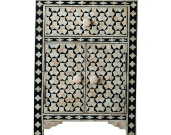 Può includere: Un mobile decorativo con un motivo geometrico. Il mobile ha un cassetto e due ante, tutti adornati da un disegno a stella nero e crema. I bordi sono rifiniti in nero e le manopole sono di colore beige chiaro.