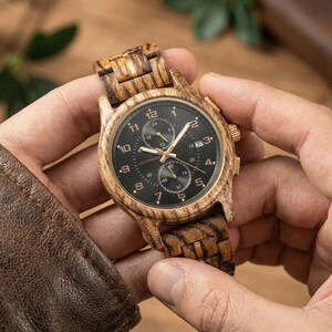Hand holding personalized wooden watch for men, front facing handmade zebrawood wrist watch gift