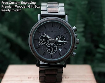 Puede incluir: Un reloj de madera oscura con esfera negra y correa de metal oscuro a juego. La esfera del reloj tiene tres esferas más pequeñas y el texto "LEATHWOOD". El reloj se muestra en una caja de madera. El texto dice "A Gift He'll Wear Every Day".