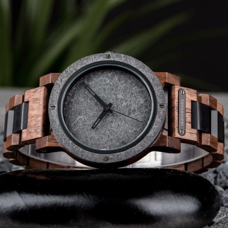 May include: A wooden wristwatch with a gray face and brown wooden band. The watch has black accents and a stainless steel clasp. The watch face has black hands and a textured appearance. The brand name "LEATHWOODS" is visible on the side of the watch.