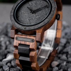 May include: Close-up of a wooden wristwatch with a dark gray face and black hands. The watch has a brown wooden frame and band with black accents. The brand name "LEATHWOODS" is visible on the watch face.