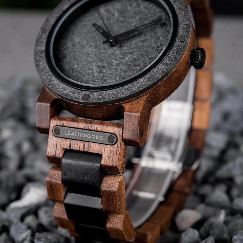 May include: Close-up of a wooden wristwatch with a dark gray face and black hands. The watch has a brown wooden frame and band with black accents. The brand name "LEATHWOODS" is visible on the watch face.